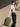 Woman holding a green backpack against a beige wall