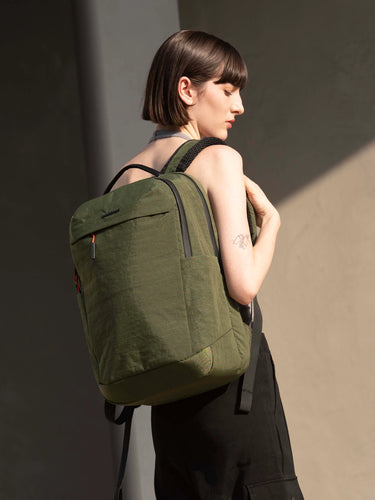 Person wearing a green backpack against a neutral background