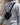 Person wearing a light gray jacket with a black sling bag over one shoulder against a blurred background.