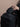 Person holding a black backpack against a beige wall