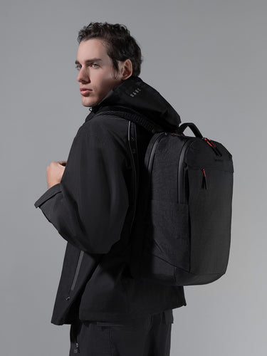 Man wearing a black backpack against a gray background