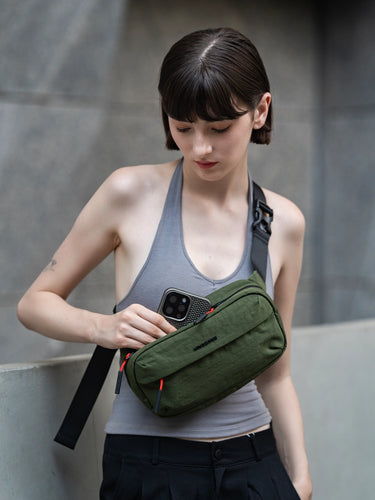 Woman wearing a green sling bag against a gray wall