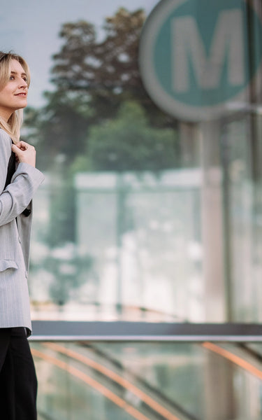 Woman with a backpack standing in an urban setting, possibly a metro station.