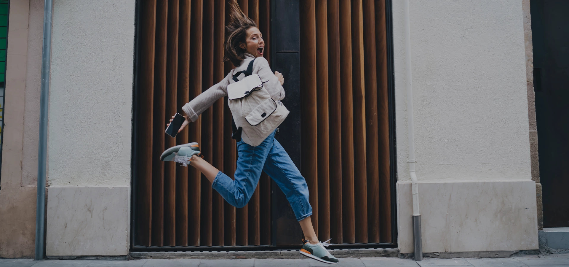 Person jumping in the air with a backpack against a building wall.