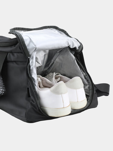 Black duffel bag with white sneakers inside on a light gray background