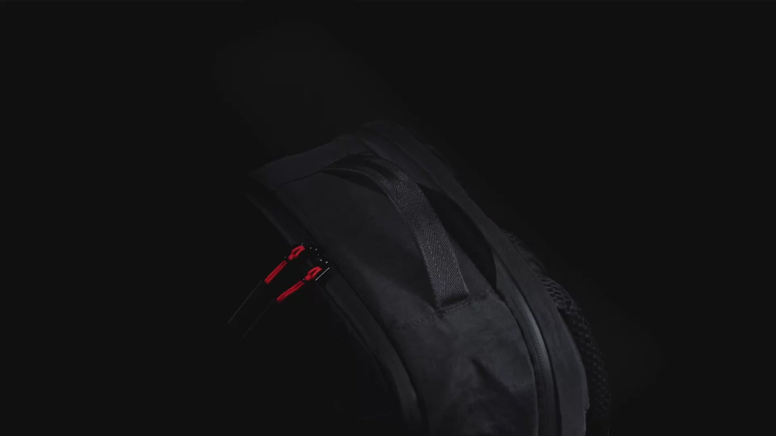 Sleek black backpack in mood lit studio. shows weather proof features 